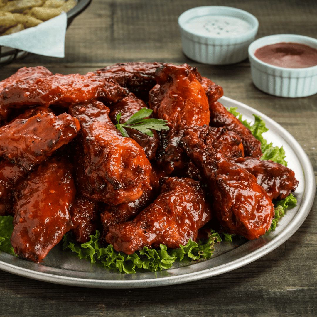 Plate of spicy, sauce-covered chicken wings served on lettuce, with an Iron Maiden receip and dipping sauces on the side.