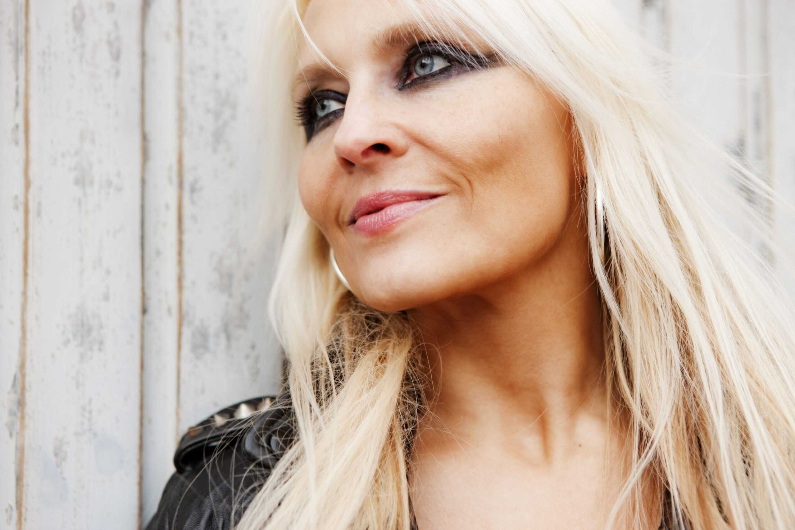 Portrait of in a black leather studded jacket, smiling confidently with one hand in her hair.
